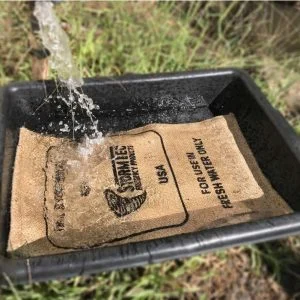 Jutesack STORMBAG in einem schwarzen Container, Wasser fällt darauf; gedrucktes Etikett mit der Aufschrift "Stormbag", Gebrauch und Datum; Produkt Karton mit 10 Säcken.