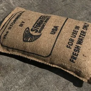 Beiger Jutesack mit dem Aufdruck "STORMBAG" mit Logo, gefaltet und auf eine dunkle Oberfläche gelegt, als Aufbewahrungs- oder Outdoor-Tasche.