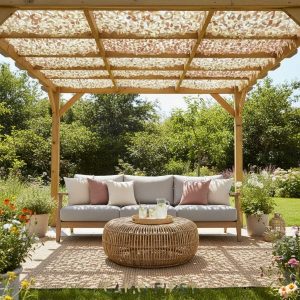 Persienne camouflage S-Cut désert 2 m x 2 m sur une terrasse ombragée; pergola en bois avec voile camouflage, canapé extérieur beige et coussins rosés, table basse ronde en osier.