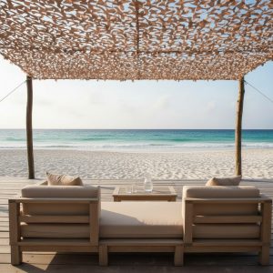 Canapé en bois sur terrasse face à la plage, ombragé par un filet camouflage beige au-dessus.