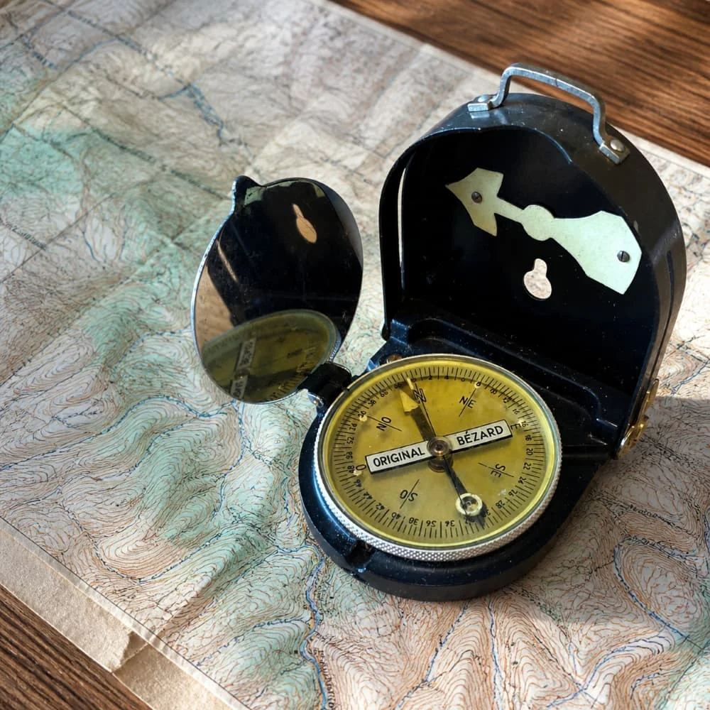 Boussole Bézard Armée Française ouverte sur une carte, cadran doré et clapet miroir, dans son boîtier noir vintage.